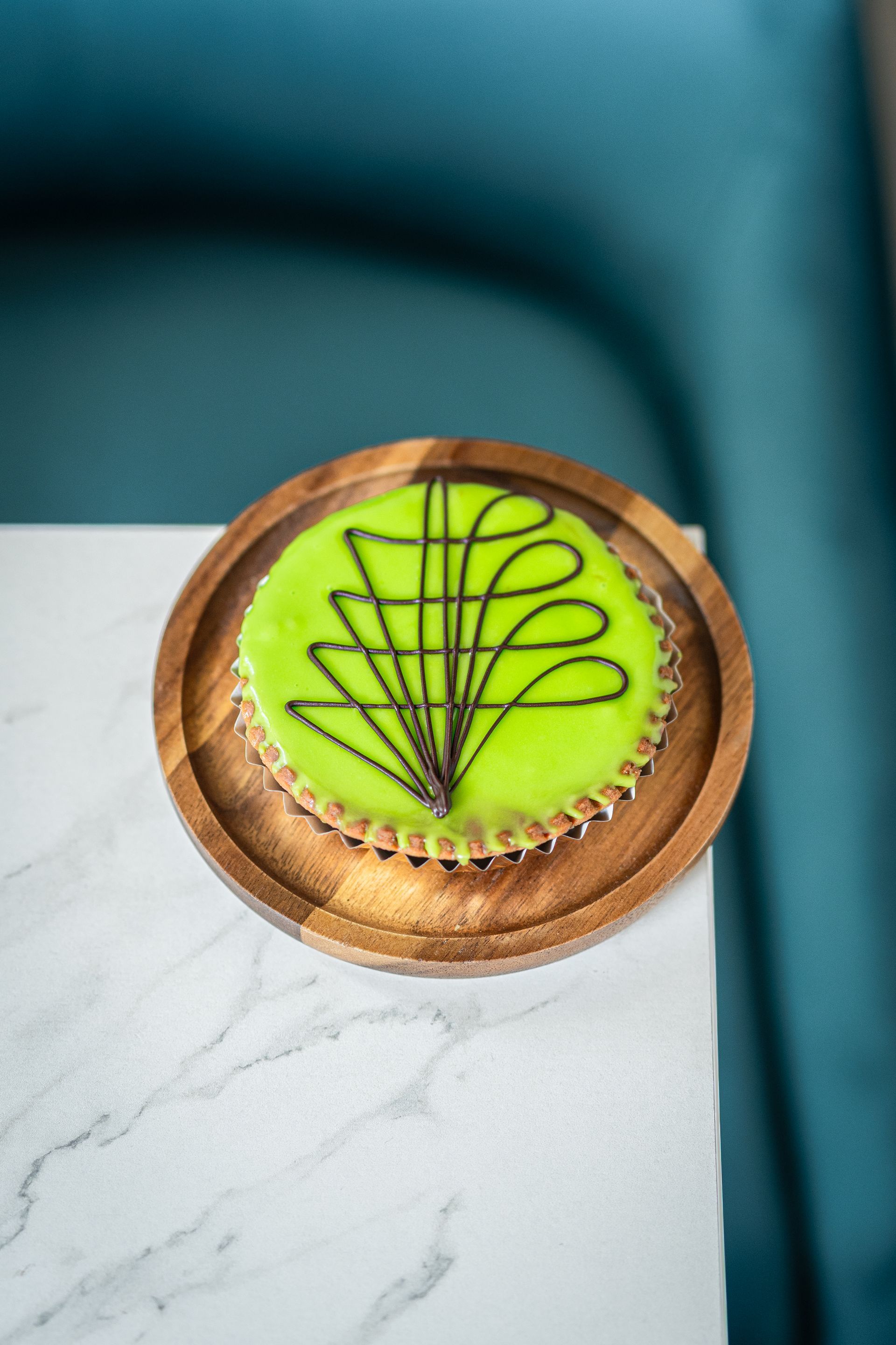 Gâteau vert vif glacé, décoré de feuilles en chocolat, présenté sur une planche en bois sur fond turquoise.