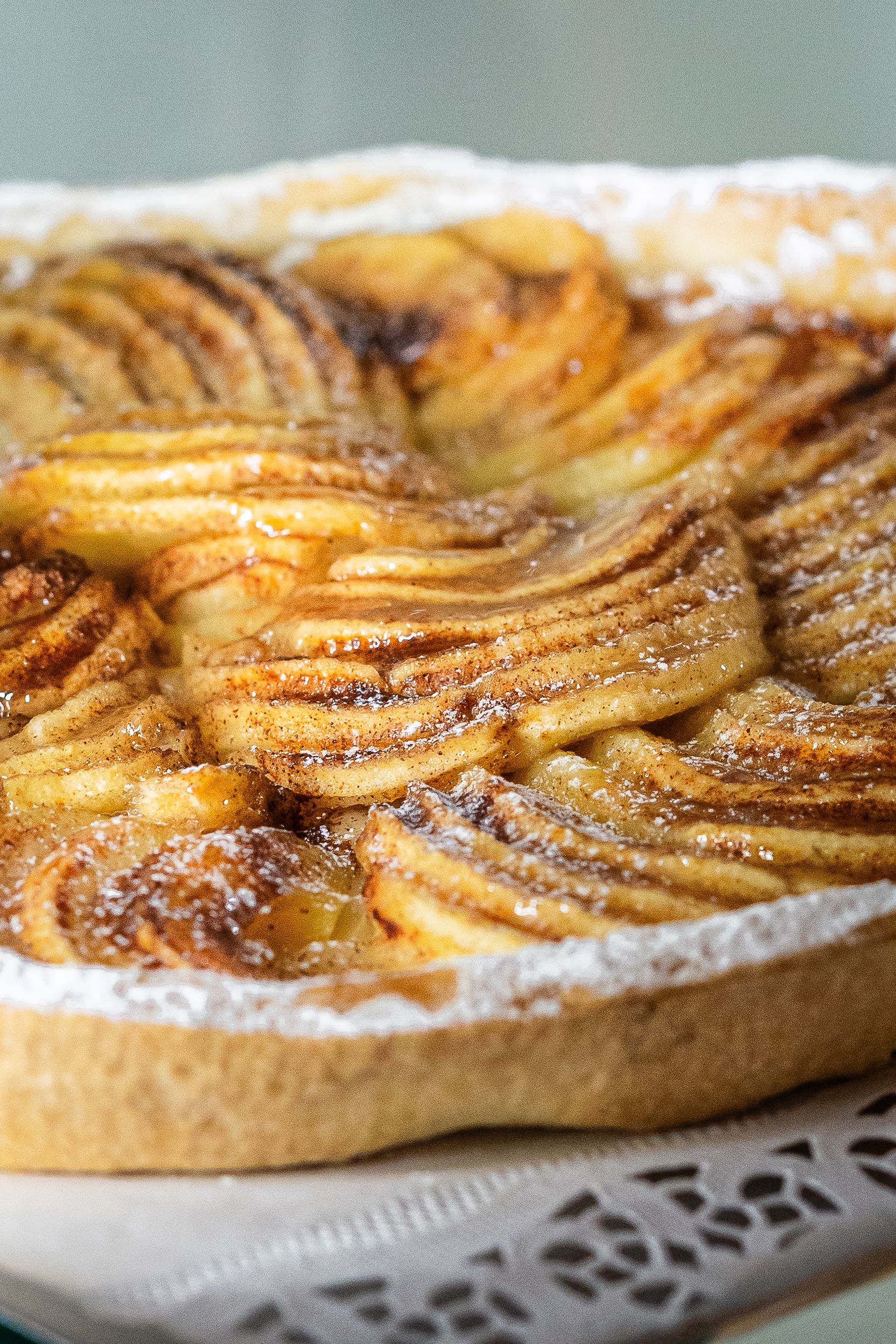 Gros plan d'une tarte aux pommes saupoudrée de sucre glace sur un napperon en dentelle, la pâte dorée remplissant le cadre.