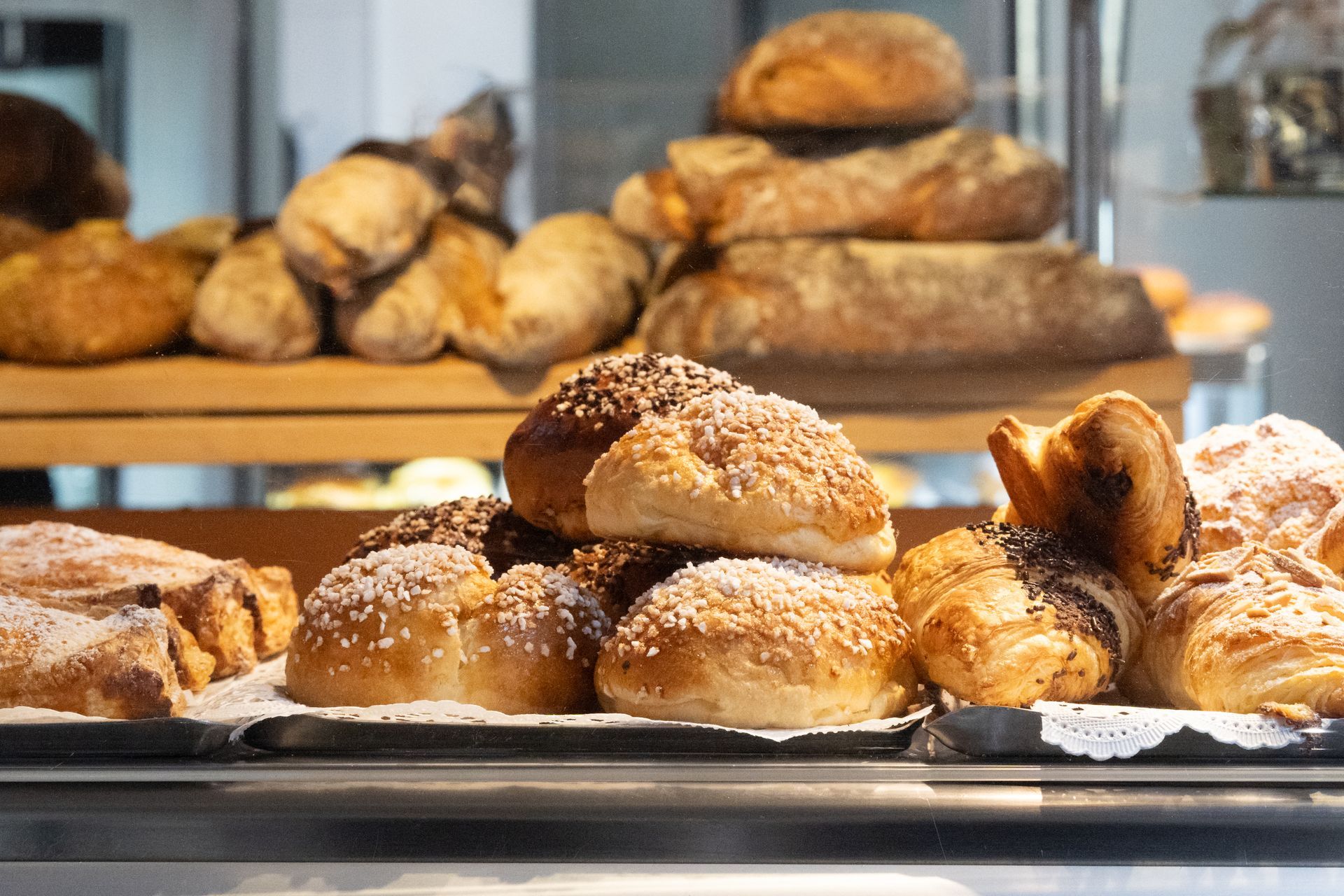 Plateau de viennoiseries assorties présenté dans une vitrine de boulangerie, avec d'autres pains en arrière-plan.