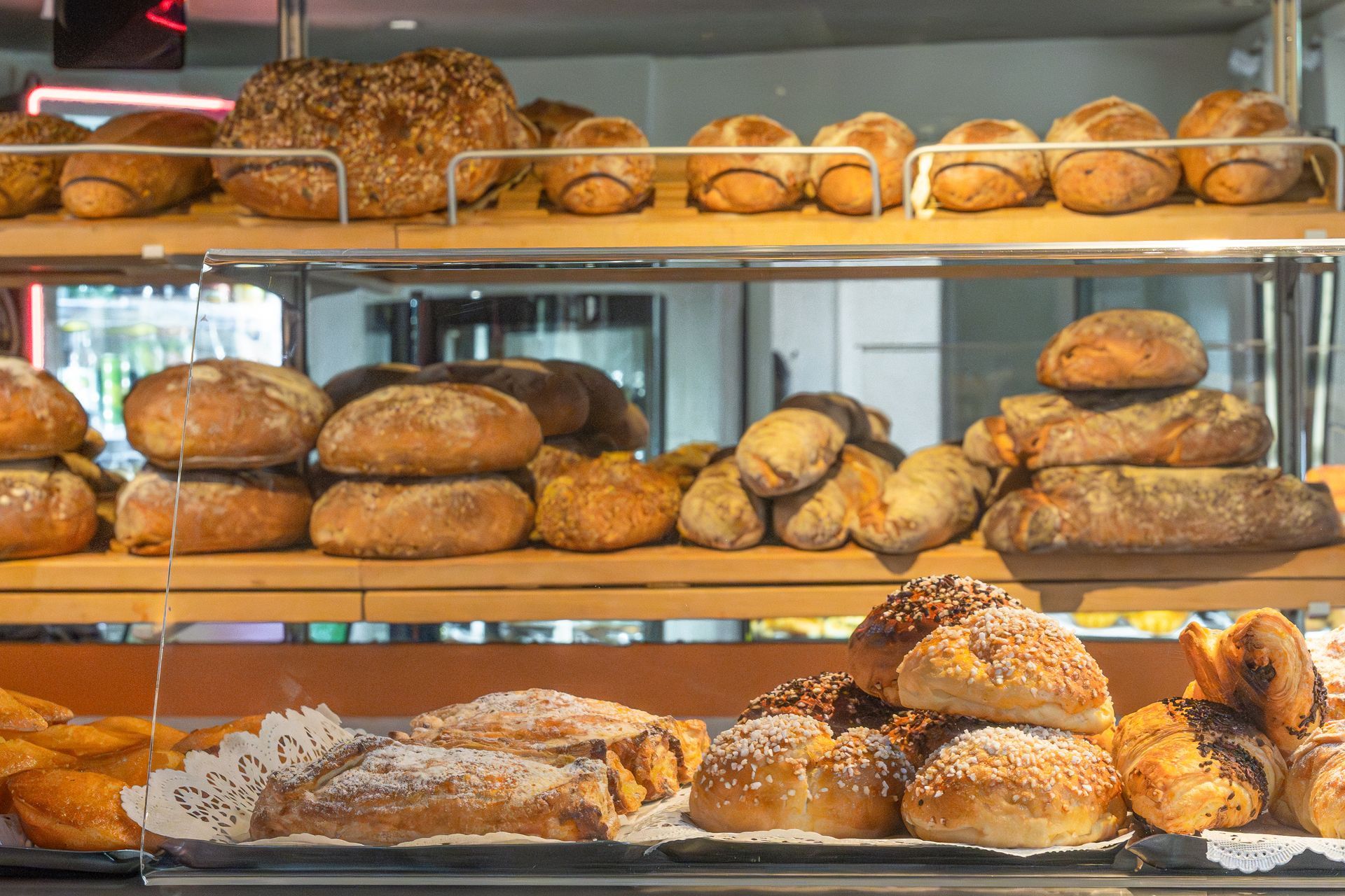 Pains et petits pains présentés sur des étagères en bois dans une boulangerie.
