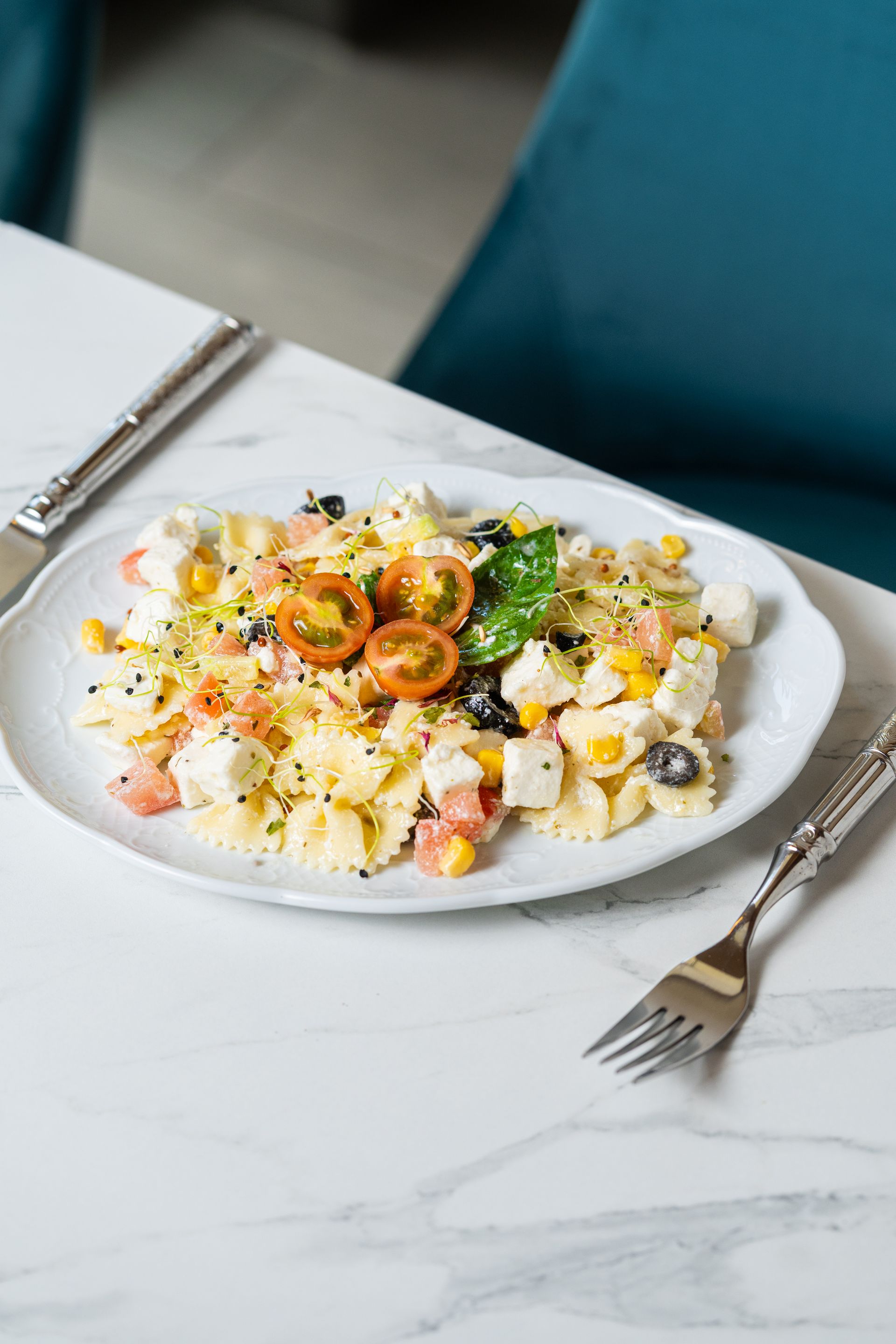 Assiette de salade crémeuse avec maïs, tomates cerises et herbes aromatiques sur une table en marbre, avec une fourchette à proximité.