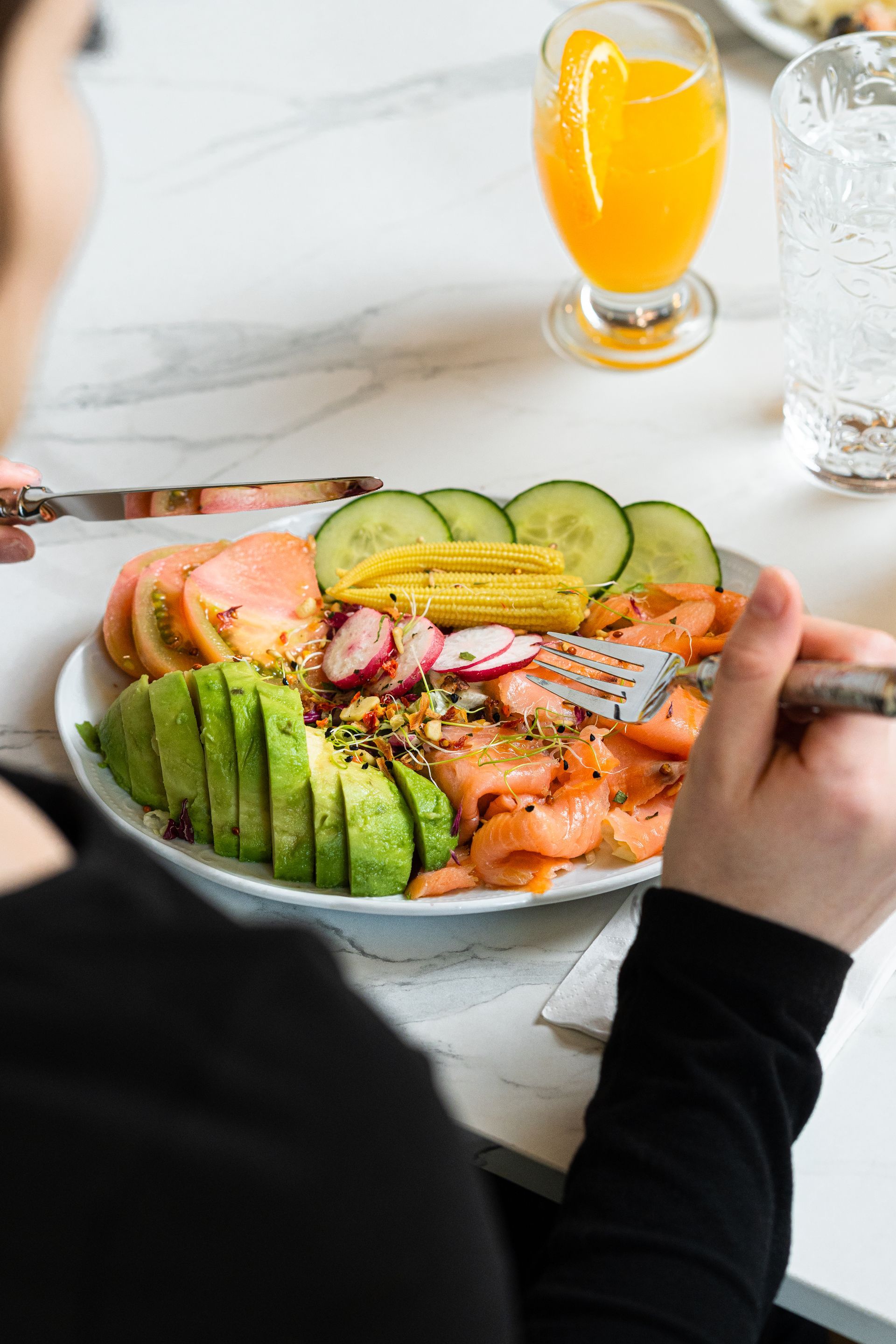 Une personne tenant un bol de saumon, d'avocat, de concombre et de cornichons à une table de petit-déjeuner colorée