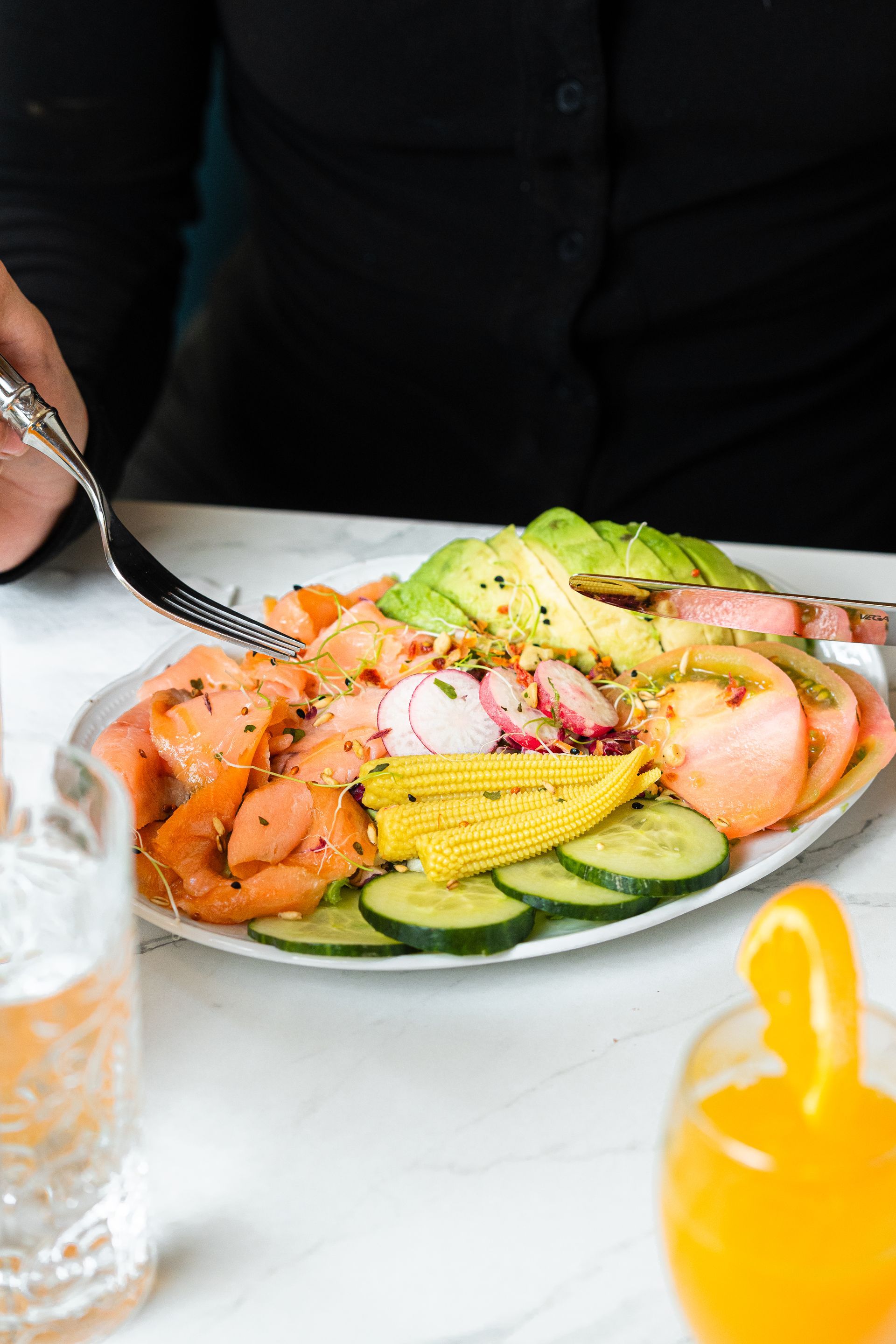 Une personne sert une salade colorée avec de l'avocat, du concombre et du saumon sur une table blanche