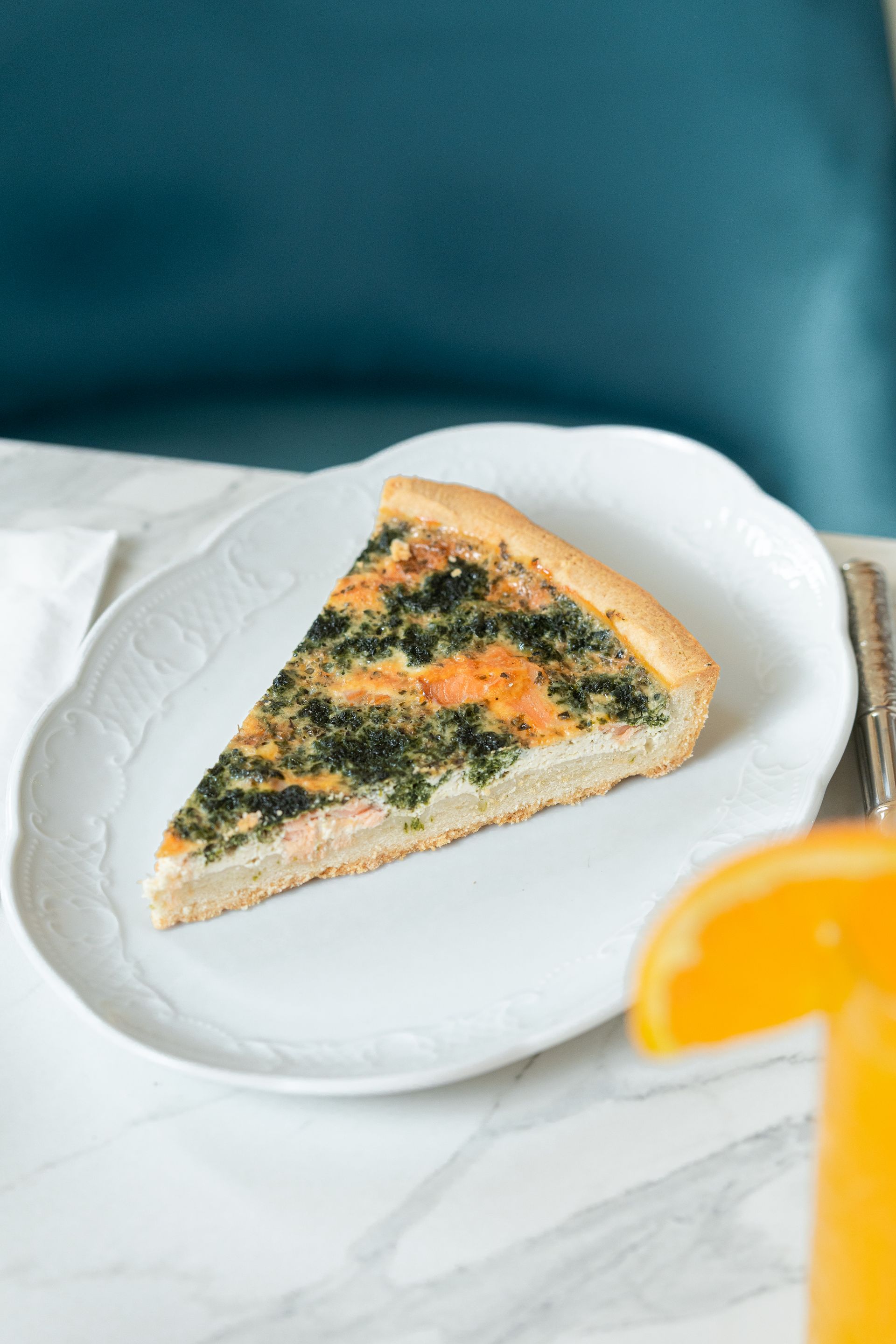 Une part de quiche salée sur une assiette blanche avec un quartier de citron sur une table en marbre