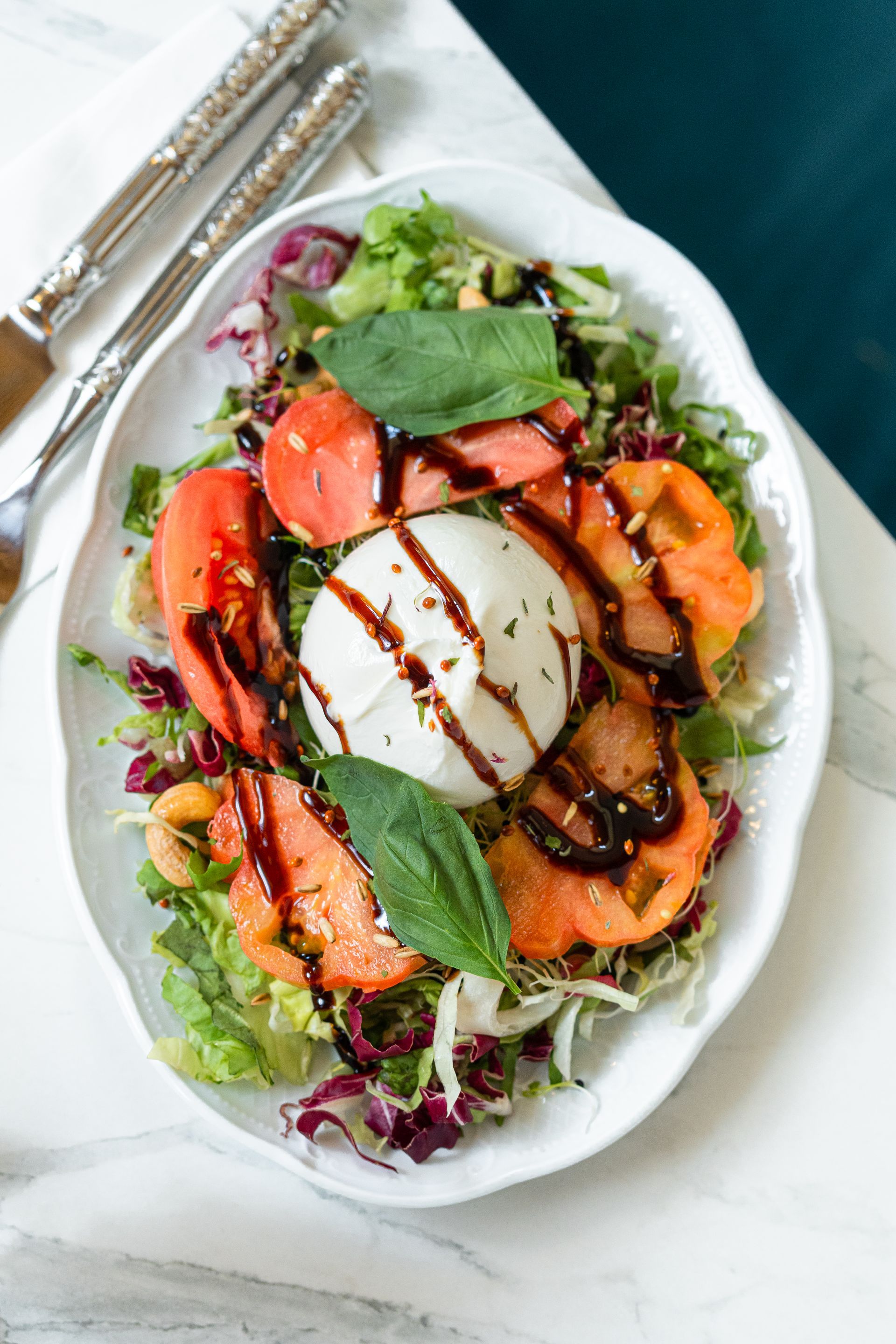 Salade de pêches grillées et de burrata sur une assiette blanche, nappée d'un glaçage balsamique et accompagnée de verdure.