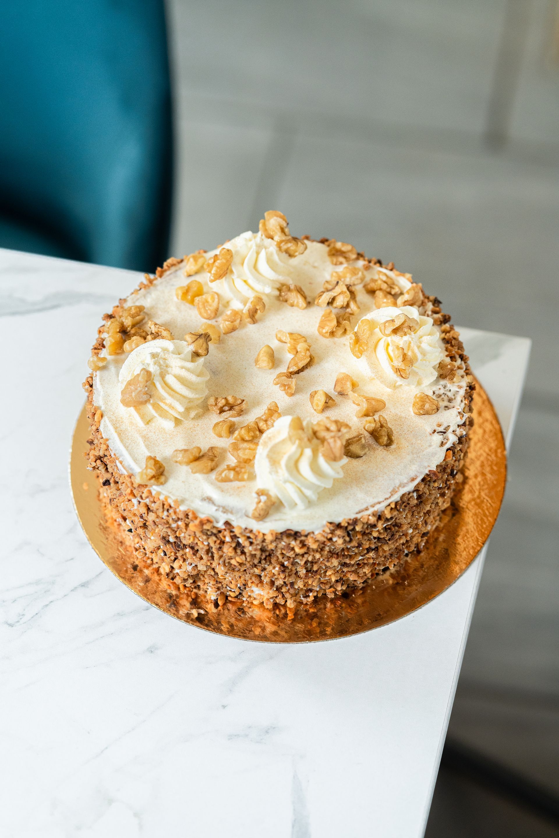 Gâteau blanc glacé avec un filet de caramel et des noix sur une table blanche près d'une chaise turquoise