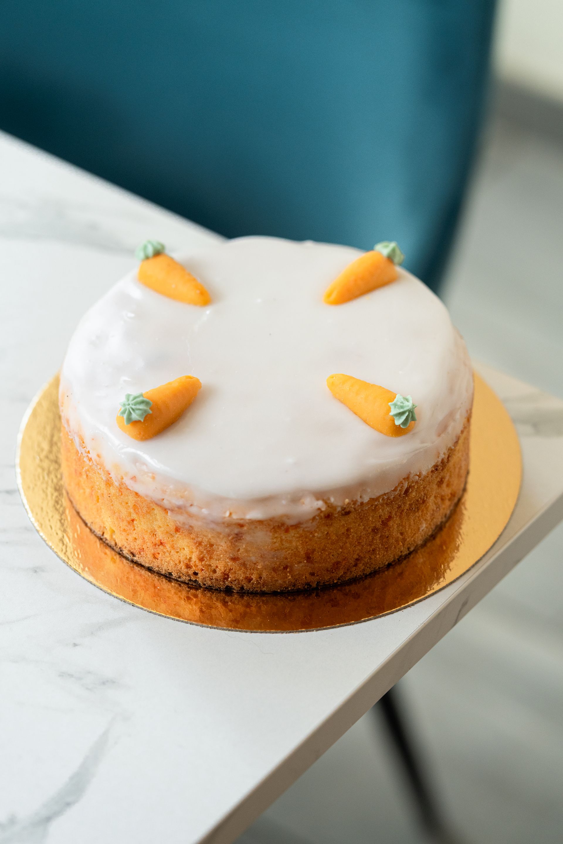 Gâteau blanc glacé décoré de petites carottes, présenté sur un plateau doré, lui-même posé sur une table blanche.