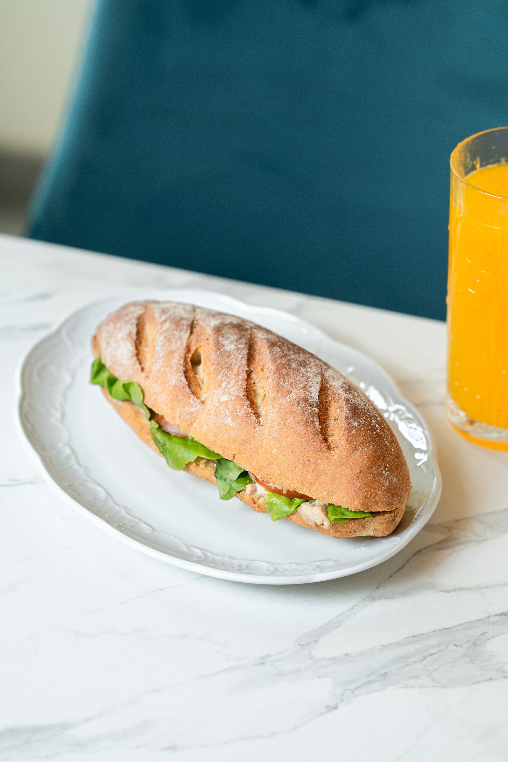 Un sandwich sur une assiette blanche à côté d'un verre de jus d'orange sur une table en marbre