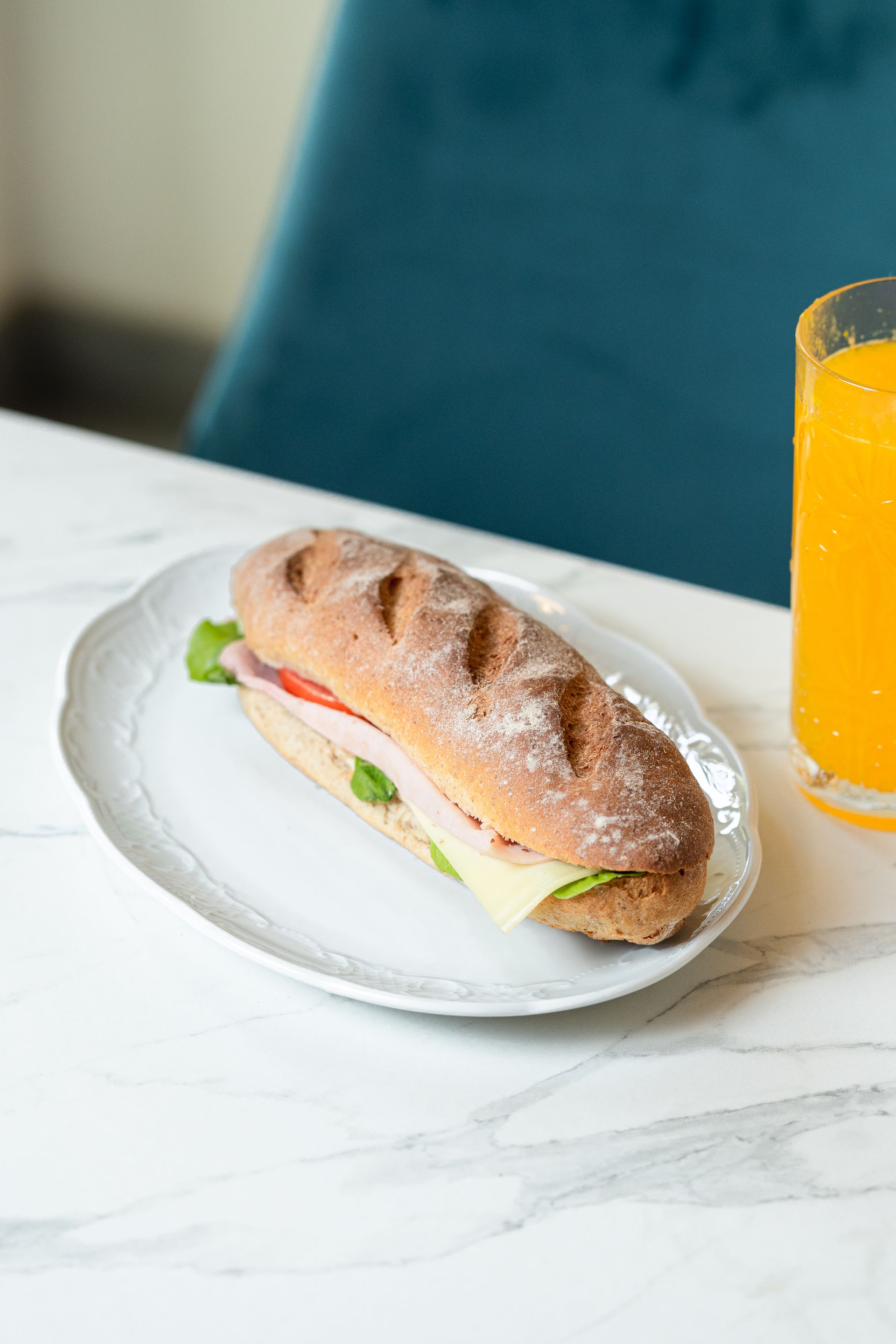 Un sandwich sur une assiette blanche à côté d'un verre de jus d'orange sur une table en marbre