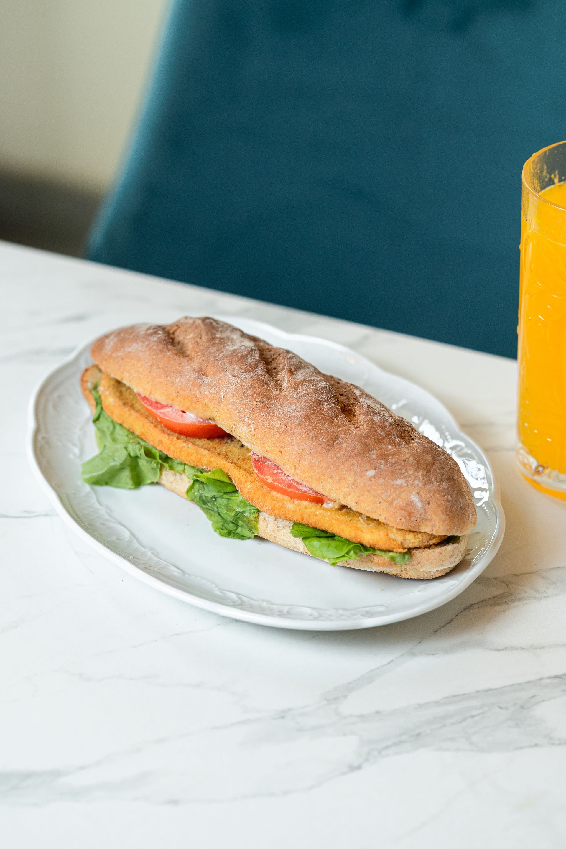Un sandwich sur une assiette blanche à côté d'un verre de jus d'orange sur une table en marbre