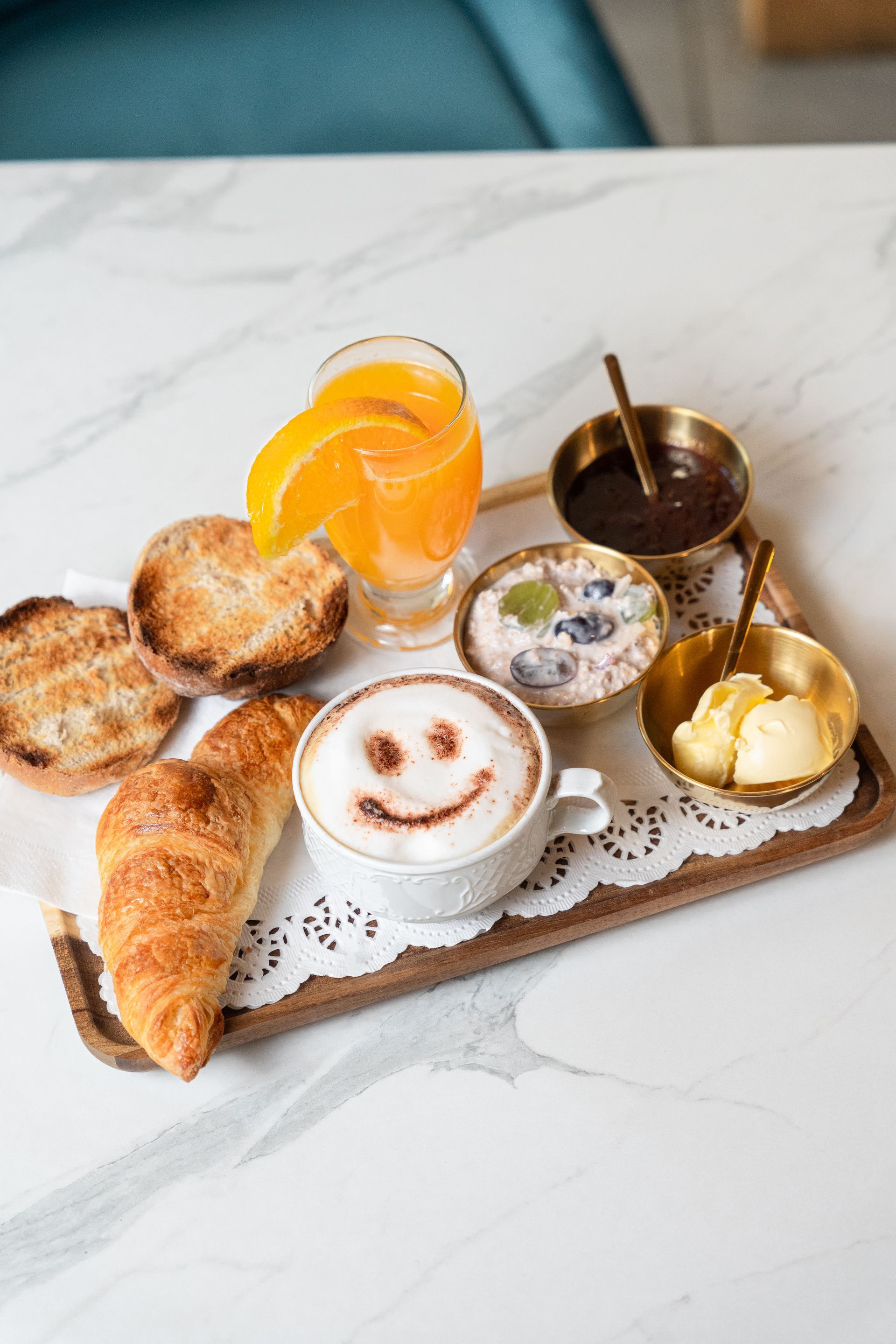 Assortiment de viennoiseries et de thé sur un plateau, avec un latte souriant et une boisson à l'orange sur une table en marbre