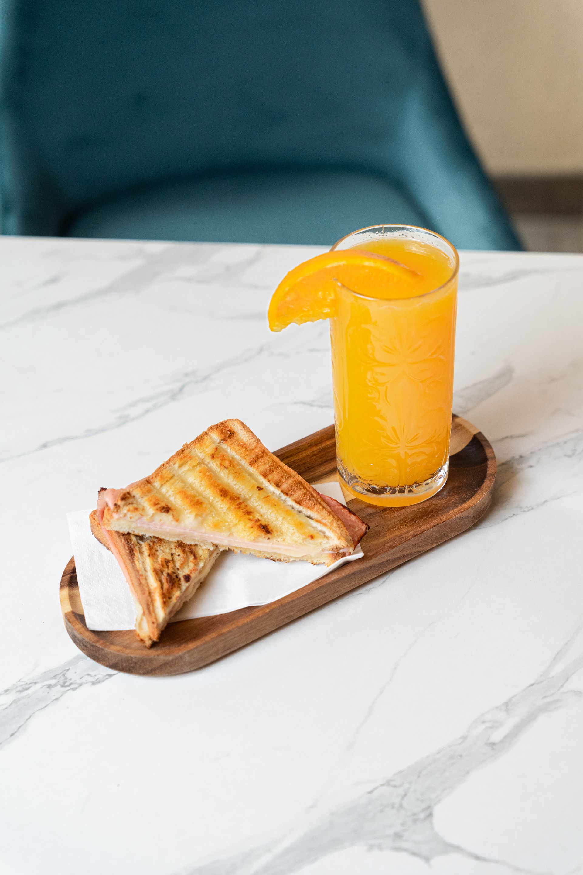 Sandwich grillé et jus d'orange sur un plateau en bois, sur une table en marbre