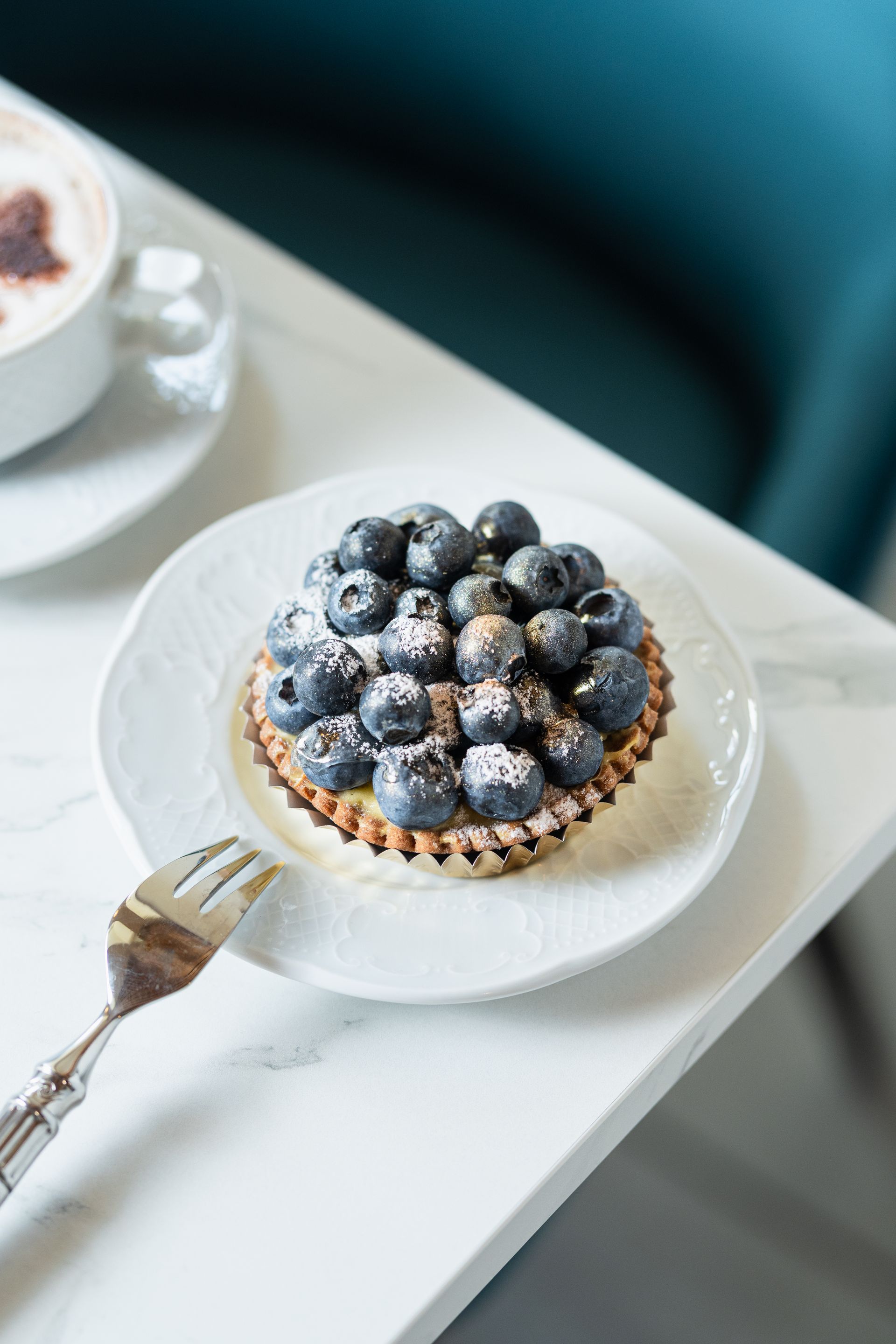 Tarte aux myrtilles sur une assiette blanche avec une fourchette dorée sur une table blanche
