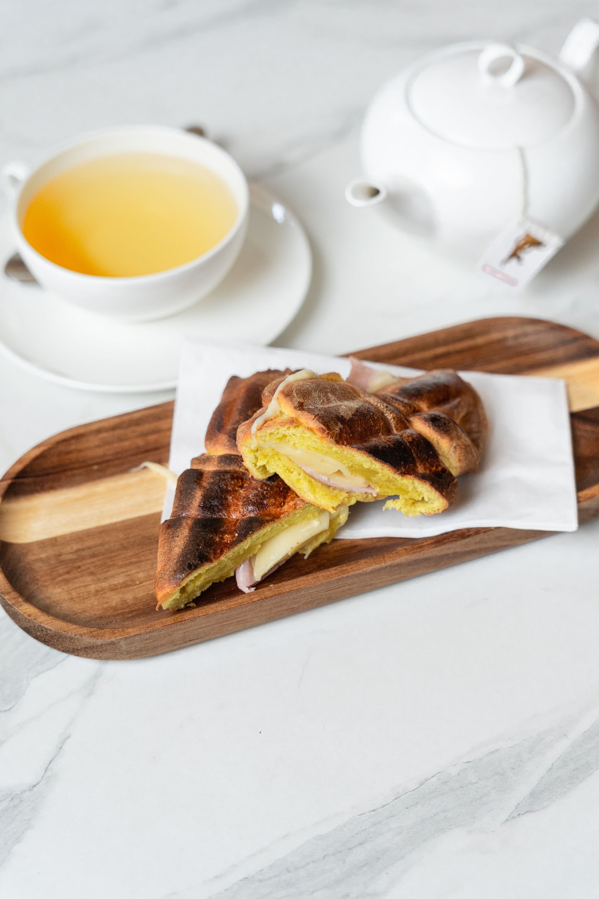 Thé accompagné d'un sandwich grillé sur une planche en bois et d'une théière blanche