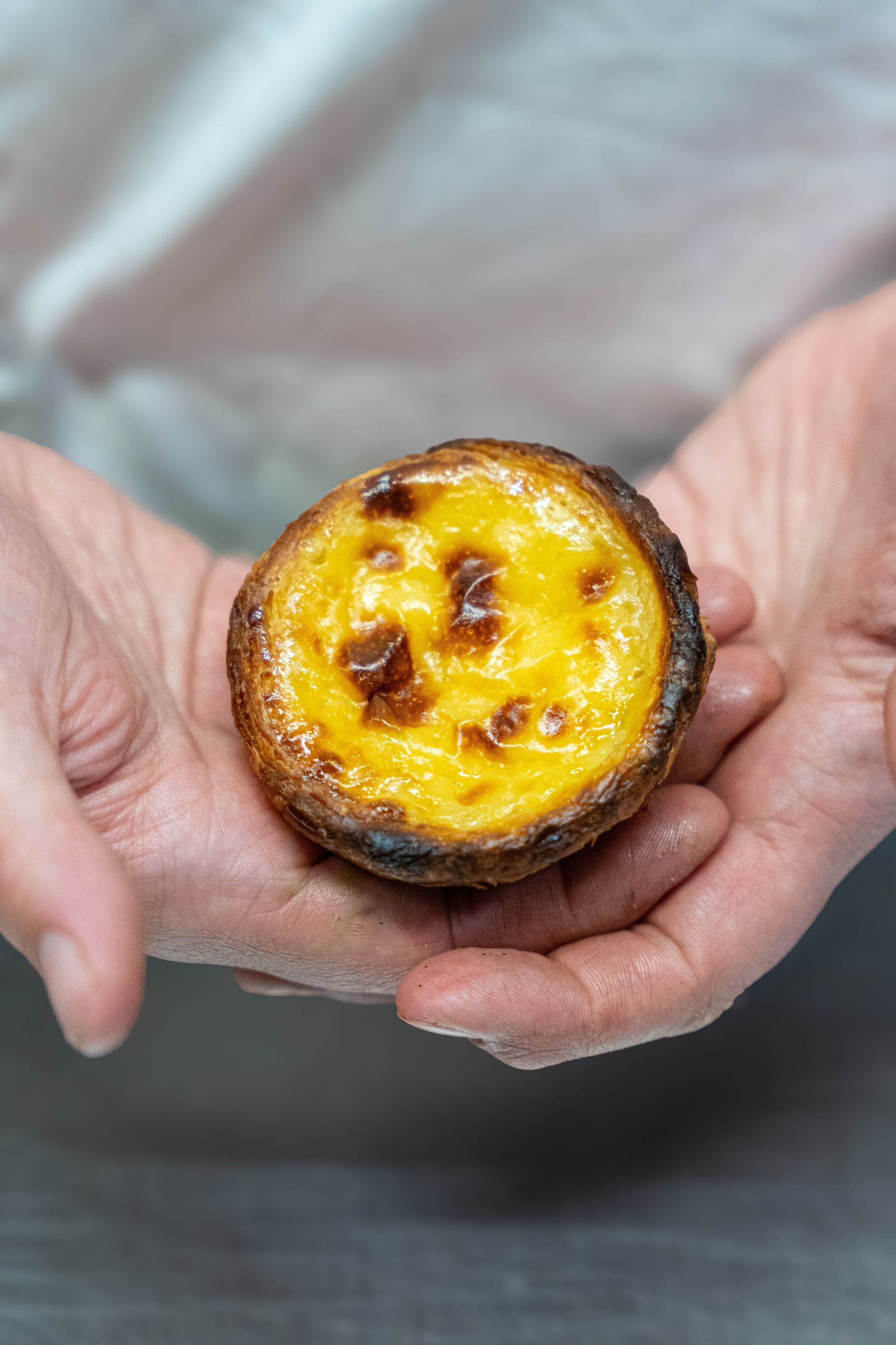 Des mains tenant une petite tartelette à la crème caramélisée avec un dessus doré