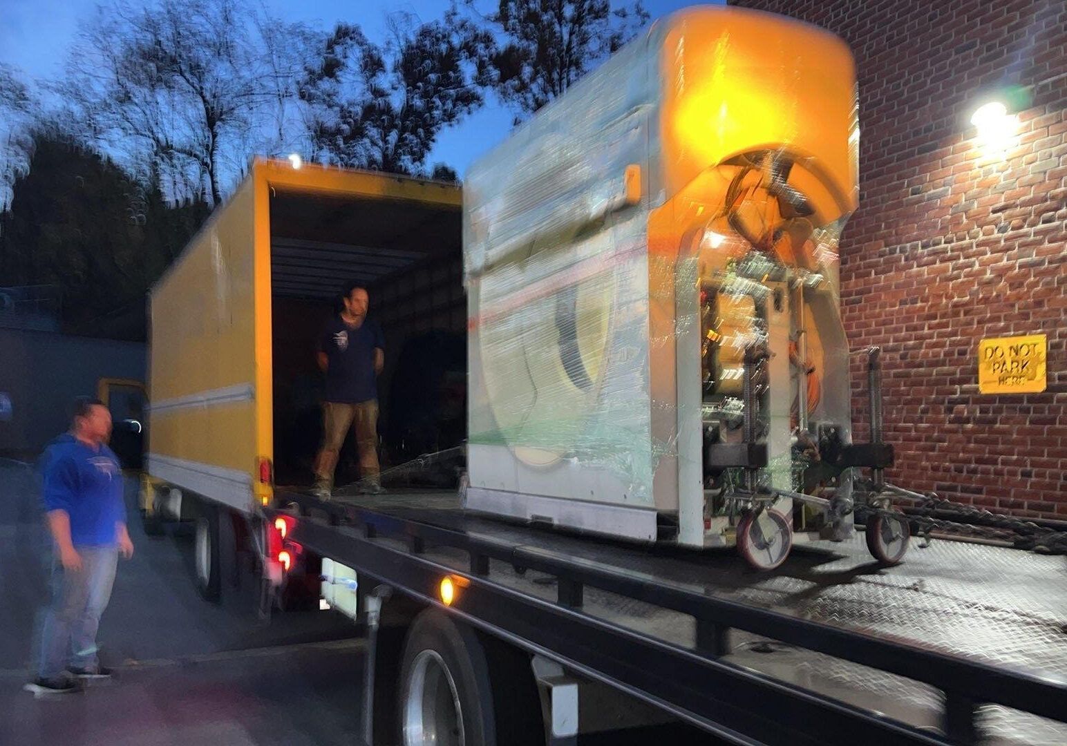 Two men loading a lawnmower into a trailer outdoors. One is guiding it, the other is assisting. Two men loading a lawnmower into a trailer outdoors. One is guiding it, the other is assisting.