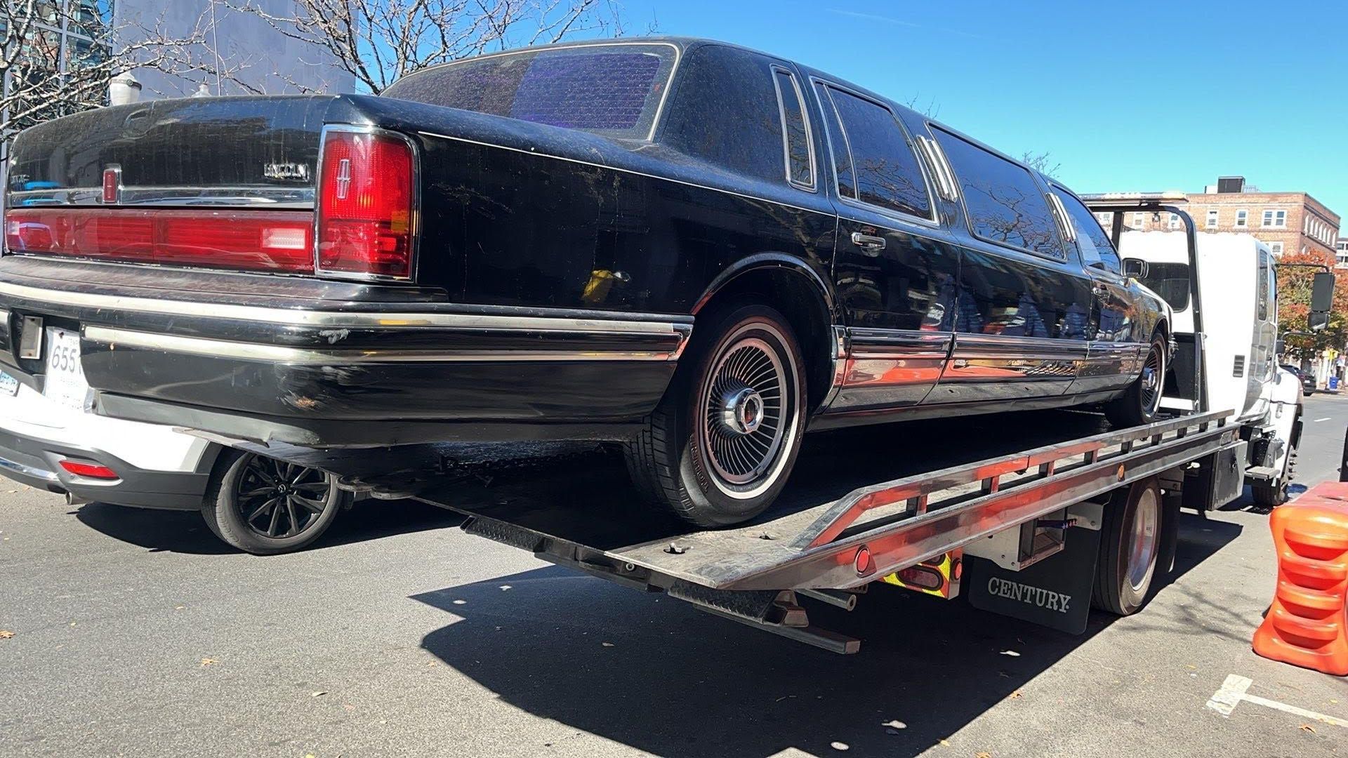 Tow truck operator loading a white car onto the flatbed; forest background. Tow truck operator loading a white car onto the flatbed; forest background.
