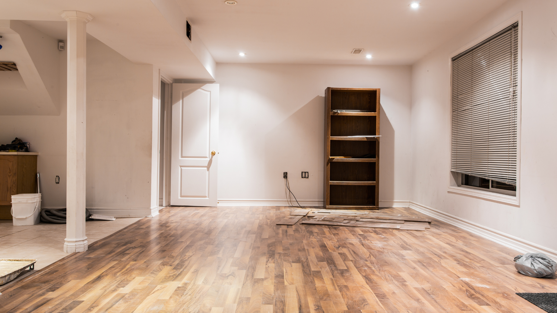 An empty basement with hardwood floors and a bookshelf.