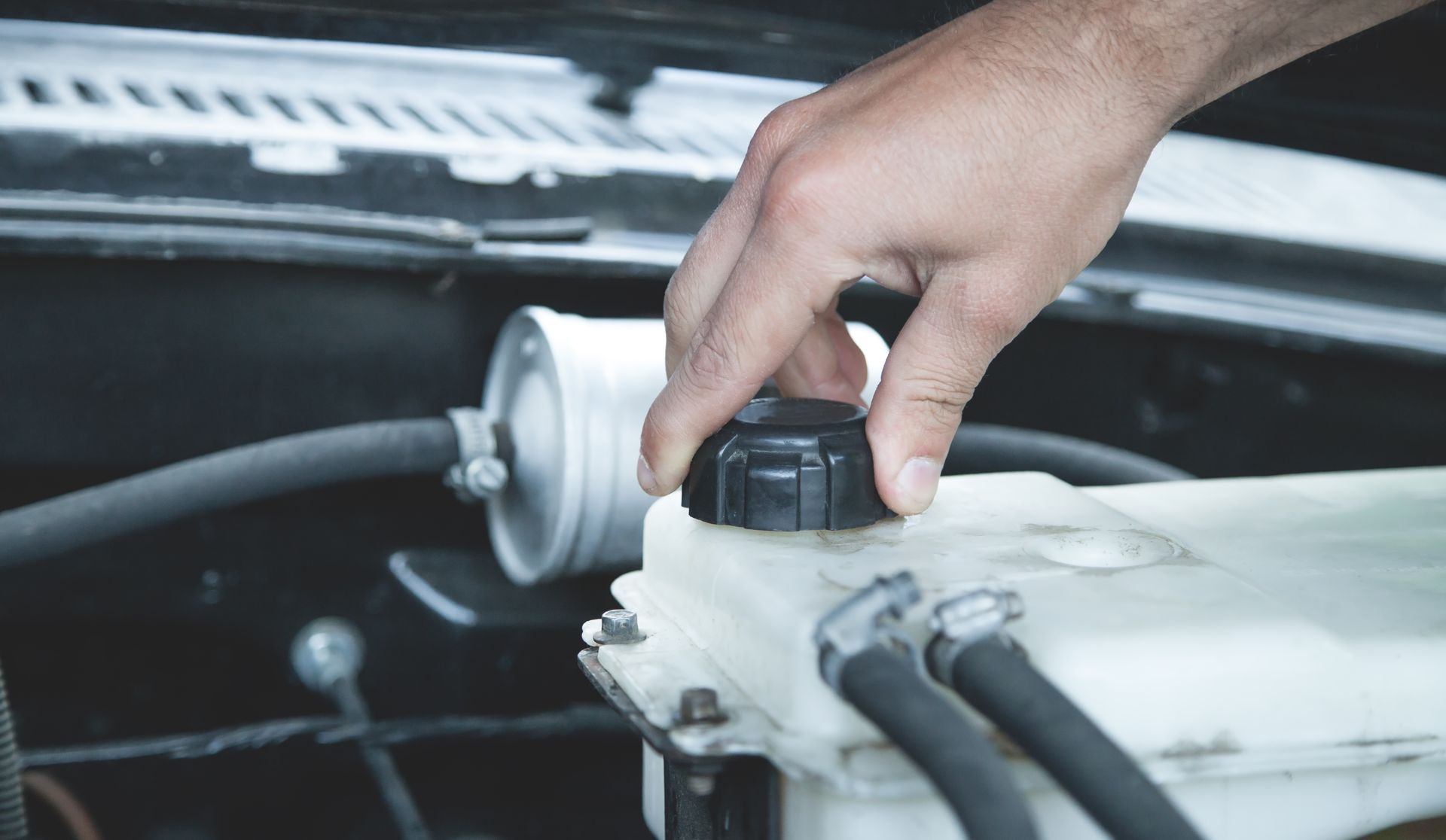 Hand opening coolant reservoir cap under a car hood.