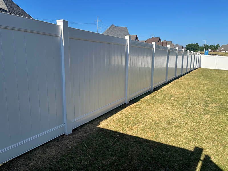 White vinyl privacy fence along a sunny suburban yard with grass and houses in the background