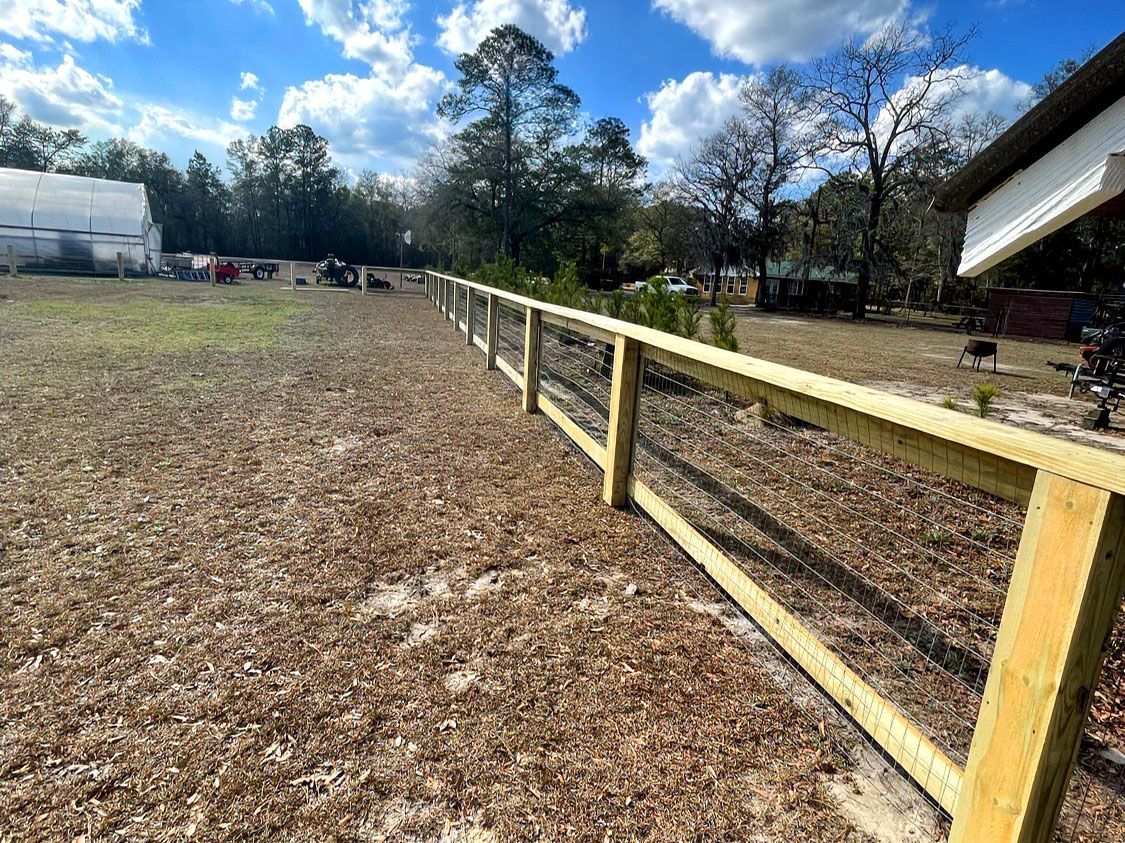 Wooden fence along a grassy field under a blue, partly cloudy sky