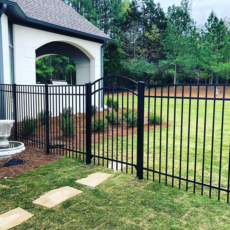 Black metal fence beside a white house archway, with a grassy yard and stone path leading to it