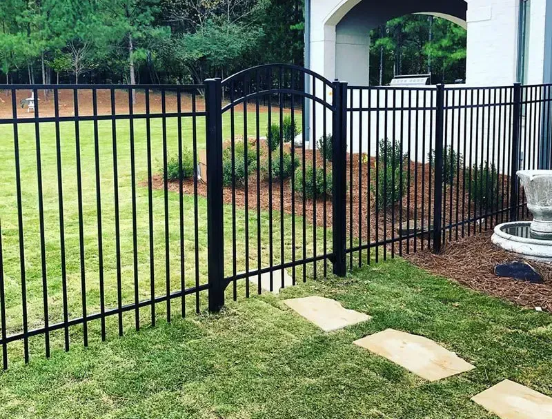 Black metal fence beside a grassy yard and stone patio steps under an archway