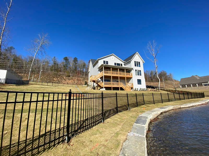 Lakefront house with a wooden deck, black fence, and blue sky beside the water