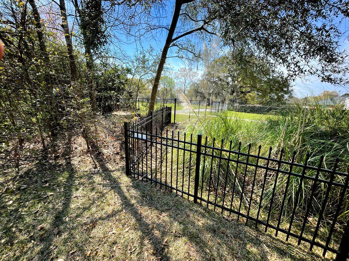 Black metal gate along a grassy path beside trees and a sunny field