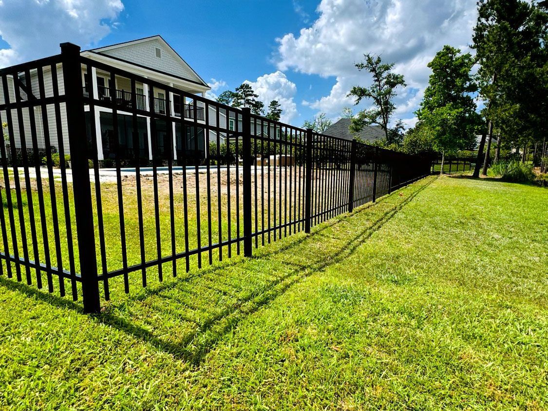 Black metal fence beside a grassy lawn and modern building under a bright blue sky