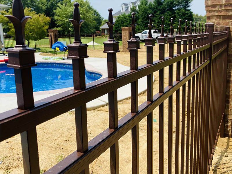 Brown metal fence beside a blue swimming pool in a sunny landscaped yard