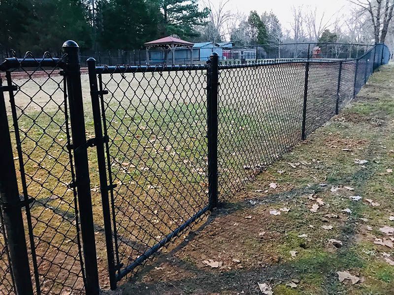 Black chain-link gate in a fenced grassy yard beside a sidewalk and houses.