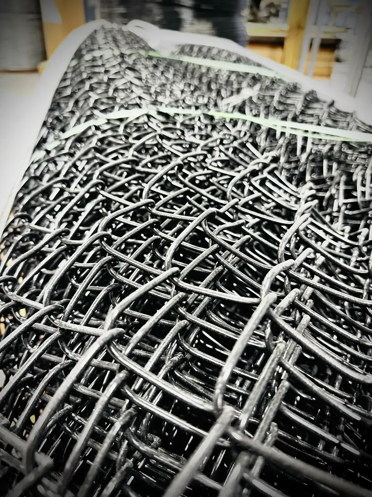 Close-up of tightly woven silver wire mesh rolled into a cylinder in a workshop or factory setting
