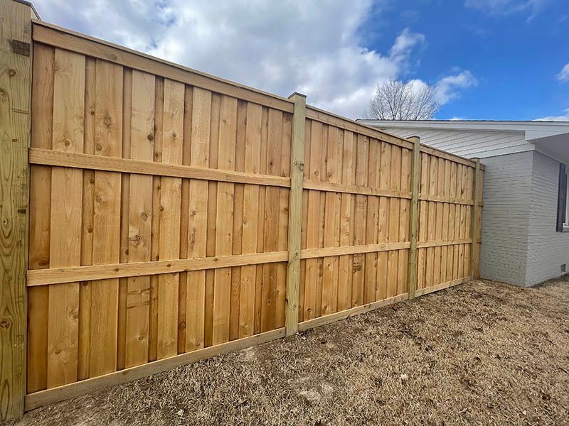 Wooden privacy fence along a gravel yard beside a white house under a partly cloudy blue sky