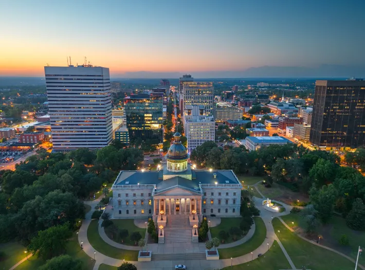 Aerial sunset view of a city skyline with a lit domed building in the foreground and office towers behind