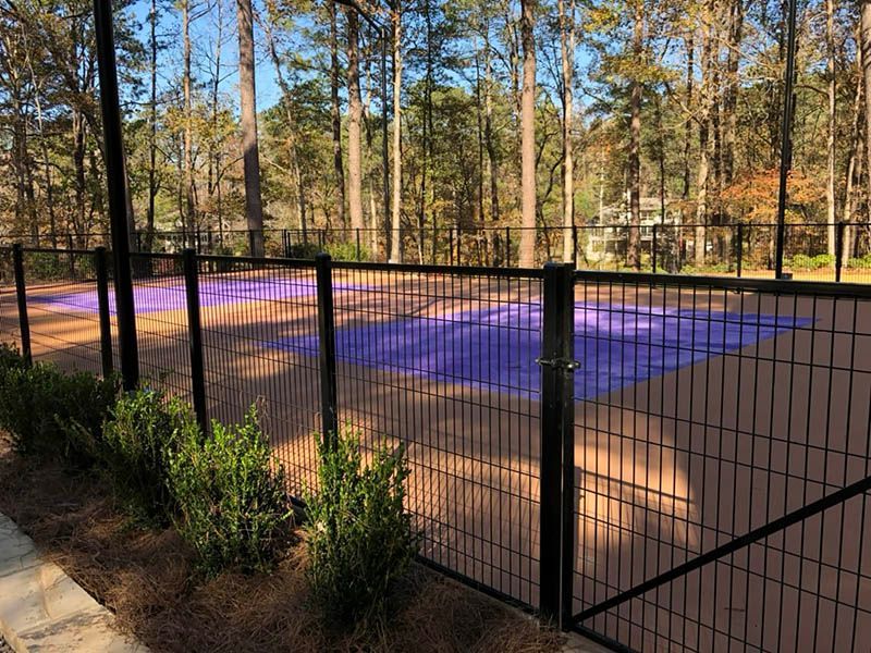 Black metal fence around a purple outdoor court in a wooded park area