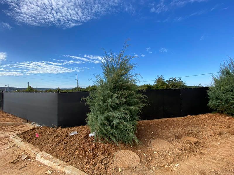 Black privacy fence with desert landscaping and two shrubs under a blue sky
