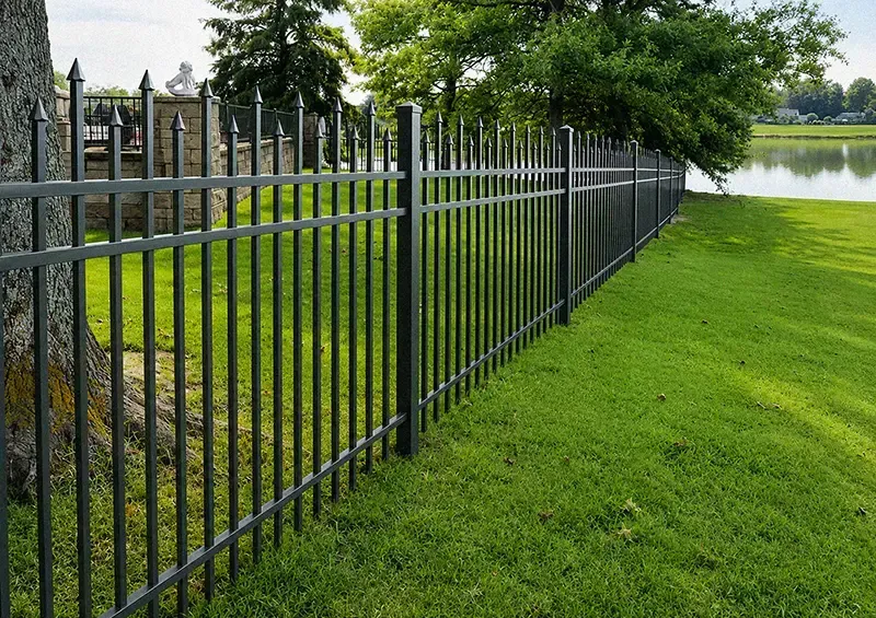 Black metal fence along a green lawn beside a lake and trees