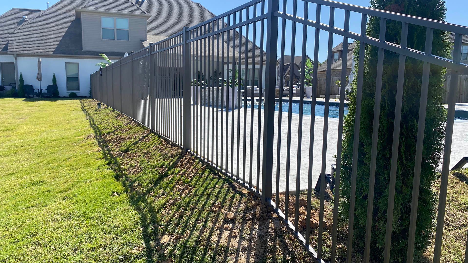 Black metal fence along a sunny suburban driveway beside a house and green lawn.