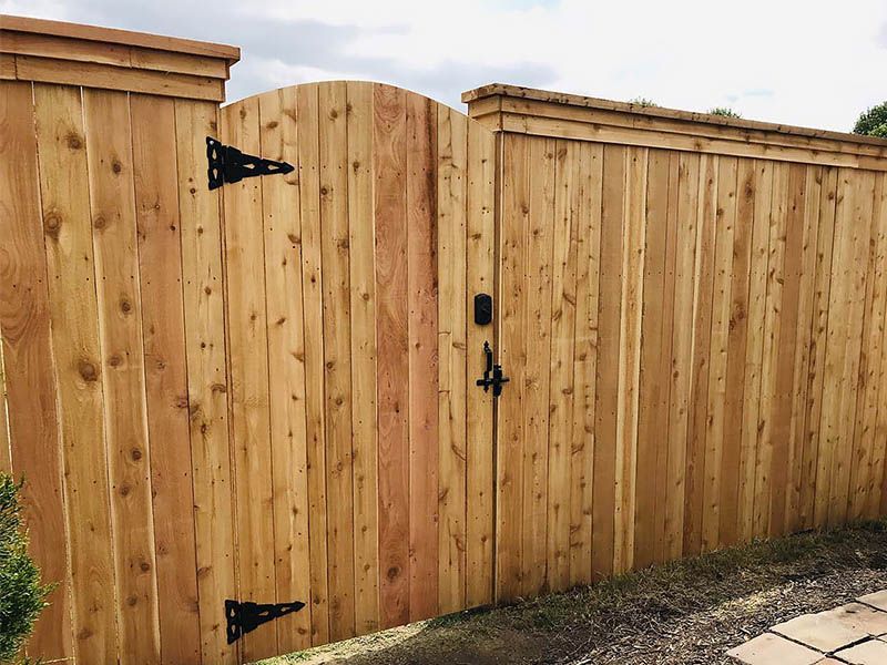 Wooden privacy gate and fence with black hinges and latch, shown in a backyard setting.