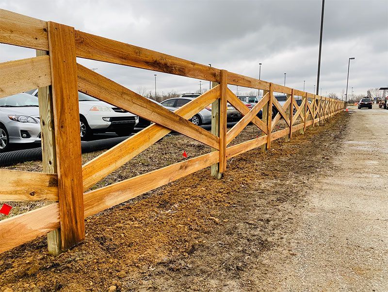 Wooden fence with diagonal braces along a parking lot beside a snowy roadside under a gray sky