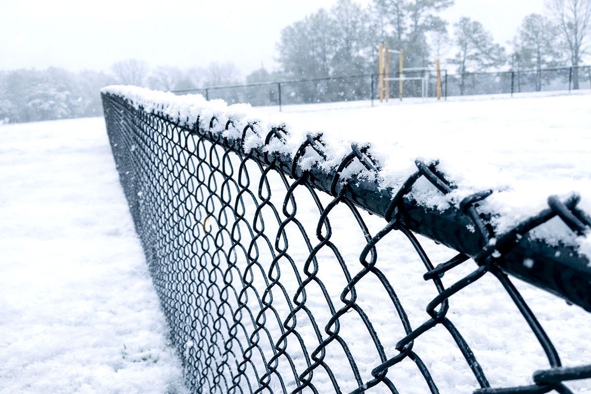 Snow-covered chain-link fence receding into a snowy field on a winter day