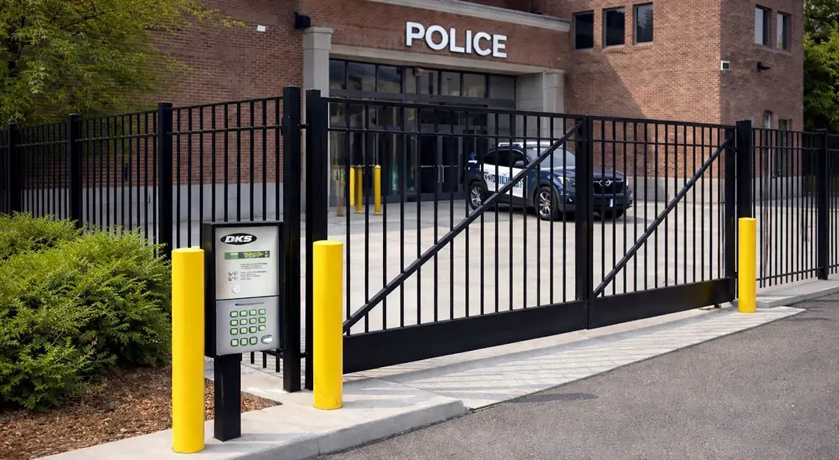 Police station entrance with black metal gate, yellow bollards, and “POLICE” sign above the door.