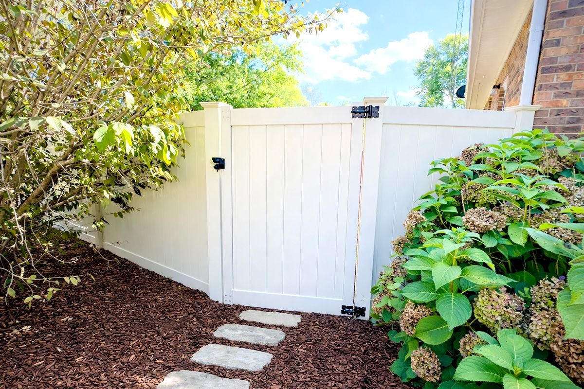 White garden gate in a lush fenced yard with stepping stones and greenery