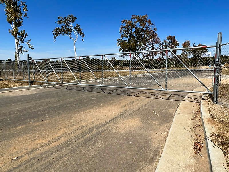 Closed chain-link gate blocking a dirt road in a rural area under a clear blue sky