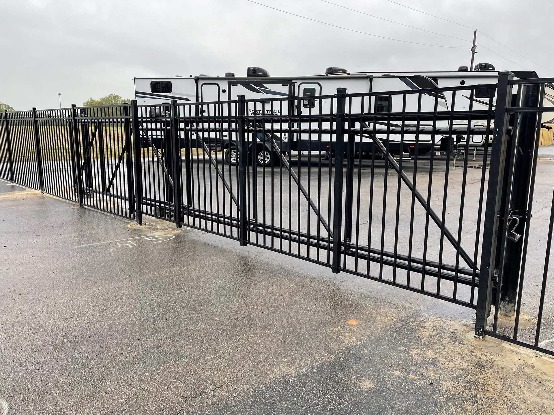 Black metal fence and gate beside a wet paved walkway on an overcast day