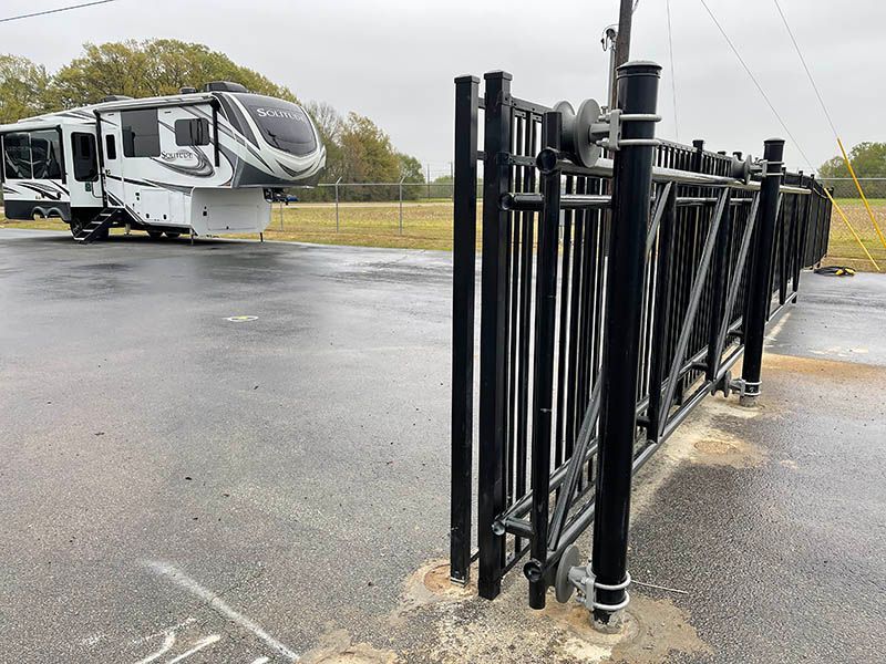 Black metal fence section beside a wet parking lot, with an RV parked in the background.