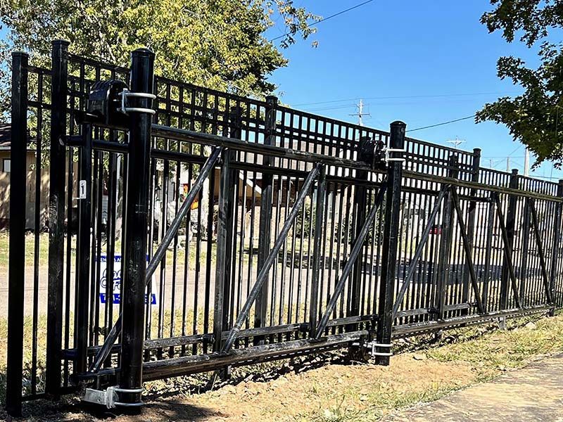 Black metal security fence with vertical bars and slanted supports along a sidewalk in daylight.