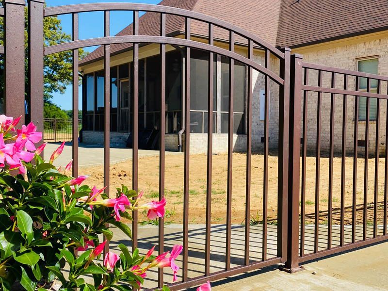 Metal gate in front of a beige building with pink flowers in the foreground.