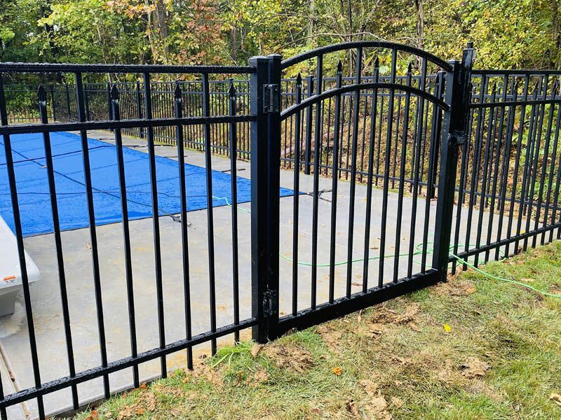 Black metal pool fence and gate beside a blue-covered pool on a concrete patio.